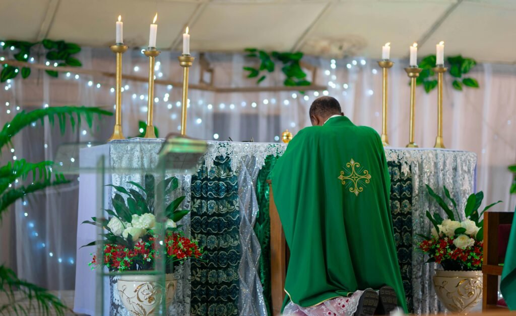 A priest in green vestments praying at a beautifully decorated church altar with candles.