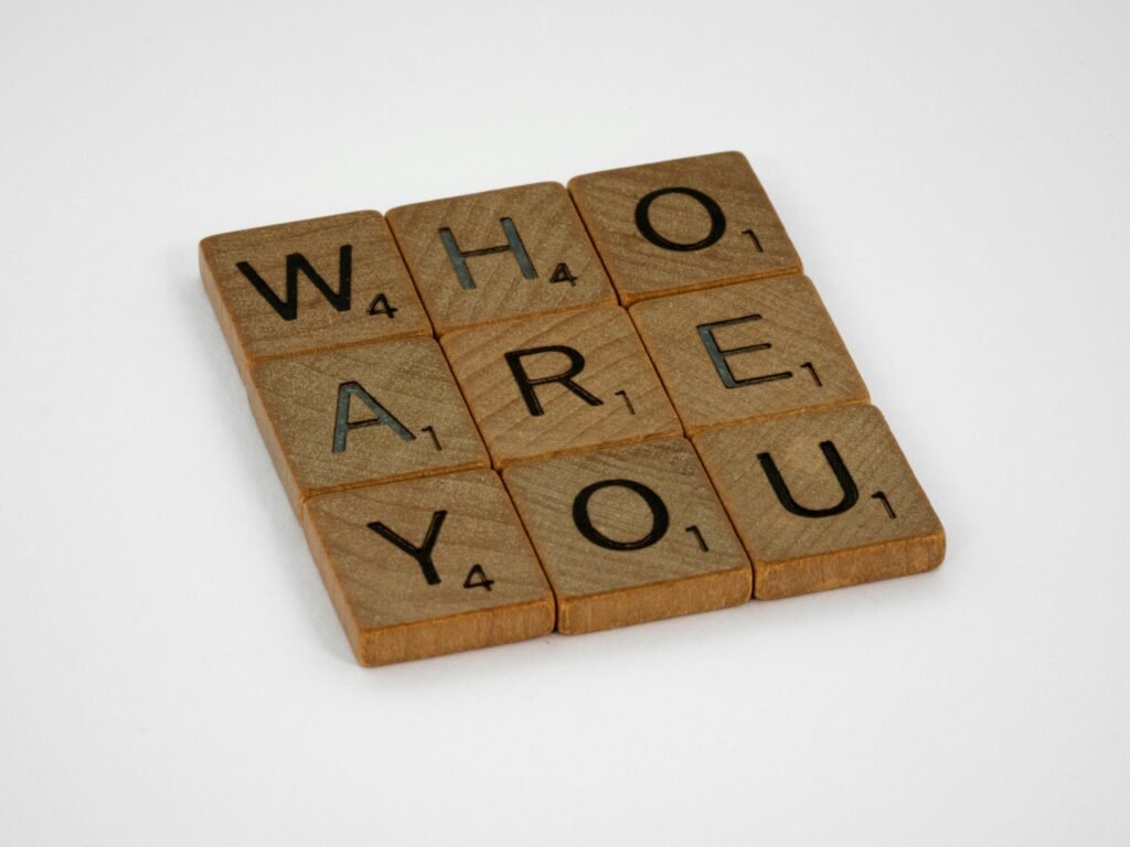 Close-up of wooden Scrabble tiles forming the phrase 'Who Are You' on a white background.