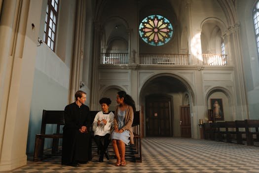 A priest in a cassock talking with two parishioners inside a church.
